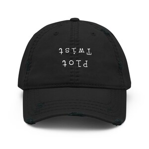 Puede incluir: Gorra de béisbol negra desgastada con las palabras "Plot Twist" bordadas en blanco. La gorra tiene una visera curva y un aspecto vintage desgastado, con bordes deshilachados.