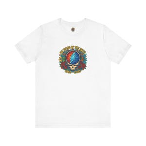 May include: White t-shirt featuring a colorful graphic celebrating 60 years of The Dead. The design includes a skull, lightning bolt, and roses, with the years 1965-2025. The shirt has a crew neck and short sleeves.