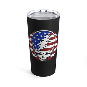 May include: A black stainless steel tumbler with a graphic of a smiling skull with an American flag design. The skull is white with black eyes and a red mouth. The flag is red, white, and blue.