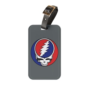 May include: Gray luggage tag with a red, white, and blue skull and lightning bolt graphic. The graphic is a stylized version of the Grateful Dead logo.