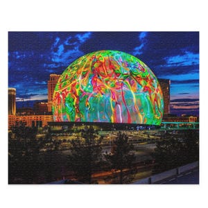 May include: A large, colorful, illuminated geodesic dome at night. The dome is surrounded by buildings and trees. The dome is lit with a variety of colors, including red, orange, yellow, green, blue, and purple.