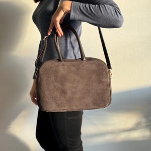 May include: A brown suede handbag with a rectangular shape, featuring a top handle and a detachable shoulder strap. The bag has a zipper closure and a minimalist design, suitable for everyday use.