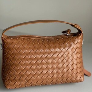 May include: A woven brown handbag with a top handle and a zipper closure. The bag has a rectangular shape and a textured surface. The handle is a matching brown color.