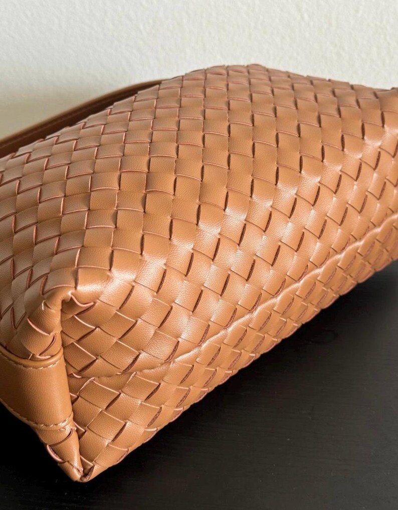 May include: A tan-colored handbag with a woven design. The bag features a rectangular shape with a shoulder strap. The woven pattern creates a textured surface, and the bag appears to be made of leather.