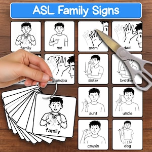 May include: A set of ASL Family Signs flashcards on a metal ring, featuring black and white illustrations of hand gestures for family members with labels like family, me, mom, dad, sister, brother, aunt, uncle, cousin, and dog, plus a pair of scissors.