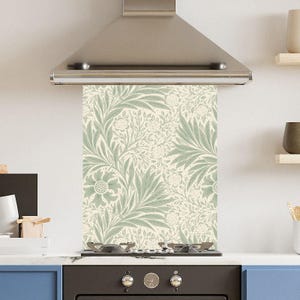 May include: A kitchen backsplash with a floral design in pale green and cream. The pattern showcases stylized flowers and leaves, offering a natural aesthetic. The backsplash is positioned behind a hob and beneath a stainless steel extractor hood.