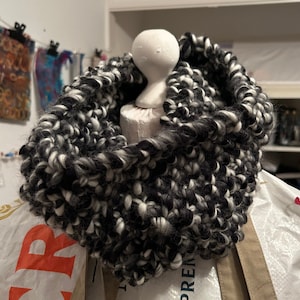 Peut inclure: Une écharpe en tricot noire et blanche en forme d'infini. L'écharpe est faite d'un fil épais et moelleux et a une texture douce et duveteuse.