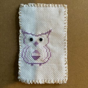 May include: A white fabric owl with purple stitching and googly eyes.