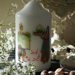 Könnte beinhalten: Weiße Säulenkerze mit einer farbenfrohen Illustration von Figuren in traditioneller Kleidung, die ein Gemälde und ein Tablett halten. Die Kerze hat Text in einer Fremdsprache. Eine dekorative Kerze.