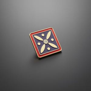 Könnte beinhalten: Quadratischer Ansteckpin mit goldenem Rand und rotem und blauem Design. Der Pin hat ein goldenes Blumenmuster mit einem kleinen, klaren Edelstein in der Mitte. Der Pin ist wahrscheinlich aus Metall und hat ein glänzendes Finish.
