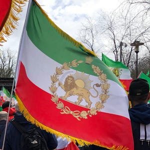 Könnte beinhalten: Eine große iranische Flagge mit grünen, weißen und roten Streifen. Der weiße Streifen zeigt ein goldenes Löwen- und Sonnenemblem. Die Flagge ist mit Gold gefranst und wird in einer Menschenmenge gehalten.