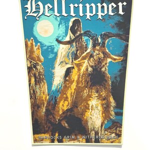 Puede incluir: Un tapiz rectangular de tela con el texto Hellripper en la parte superior y Warlocks Grim & Withered Hags en la inferior. El gráfico muestra una figura encapuchada con una capa blanca junto a una cabra grande bajo un cielo azul iluminado.