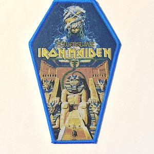 Op de afbeelding: Een blauwe, doodskistvormige patch met de tekst "Powerslave Iron Maiden" in gele letters. De patch toont een mummie en een Egyptische scène in blauw, bruin en goud. Het heeft een blauwe rand. Ongeveer 10 cm hoog.