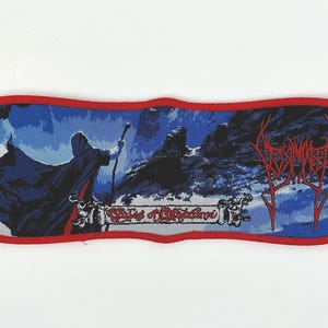 Puede incluir: Un parche tejido rojo, blanco y azul con el nombre de la banda "Summoning" y el título del álbum "Oath of Anathema" en letras rojas. El parche presenta un fondo azul oscuro con una figura con una túnica oscura y un paisaje montañoso.