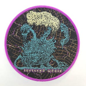 May include: Round patch with a purple border featuring a teal and black creature design with the text "tortured whole". The design has a textured appearance with a light beige cloud-like shape at the top.