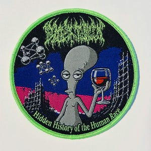 May include: A circular embroidered patch with a bright green stitched border. The design features a grey alien holding a glass of red wine against a blue and pink background. Above the alien is illegible green text, and below is the text "Hidden History of the Human Race" in green.