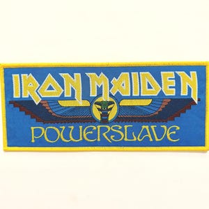 Könnte beinhalten: Ein blauer und gelber gestickter Patch mit dem Text "IRON MAIDEN" und "POWERSLAVE" und einem geflügelten Schlangenmotiv.