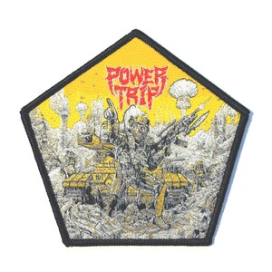 Puede incluir: Parche bordado con fondo amarillo y borde negro. El parche presenta una ilustración detallada de una figura con uniforme militar, con el texto "POWER TRIP" en rojo. El diseño incluye imágenes de guerra y explosiones.