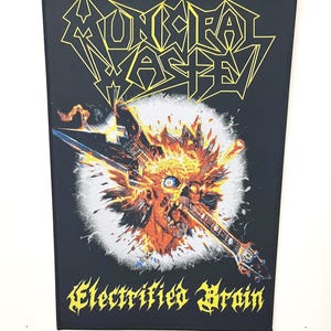 Könnte beinhalten: Ein schwarzer Patch mit dem Bandnamen "Municipal Waste" in gelben Buchstaben. Der Patch zeigt einen Schädel, der von einer Gitarre durchbohrt wird, umgeben von Flammen. Der Text "Electrified Brain" befindet sich unter dem Bild.