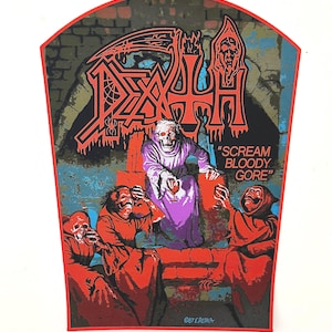May include: A red, black and white embroidered patch featuring the band name "DEATH" in large, bold letters. The patch depicts a hooded figure seated on a throne, surrounded by other hooded figures. The text "SCREAM BLOODY GORE" is printed on the patch.