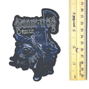 May include: A black and blue embroidered patch featuring a Grim Reaper figure with a scythe. The patch has the text "Storm of the Light's bane" in a stylized font. The patch is approximately 4 inches tall.