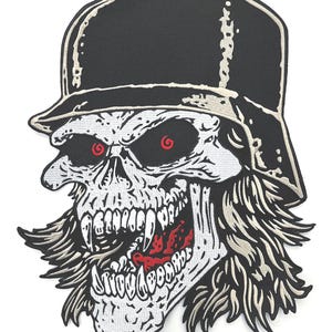Könnte beinhalten: Ein gestickter Aufnäher mit einem Totenkopf, der einen schwarzen Helm trägt. Der Totenkopf hat rote Spiralaugen, scharfe Fangzähne und langes Haar. Das Design besteht aus schwarzem, weißem und rotem Garn und zeigt ein detailliertes Skelettgesicht.