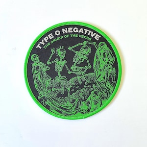 May include: A black and green embroidered patch with the text "Type O Negative The Origin of the Feces" and a graphic of skeletons.
