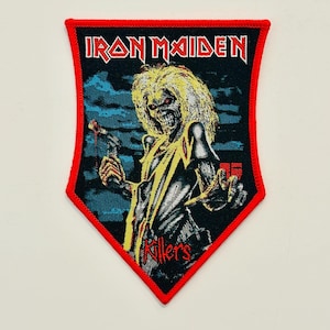 Puede incluir: Parche bordado con el logotipo de Iron Maiden y la palabra "Killers". El parche tiene un borde rojo y representa una figura esquelética con pelo largo y amarillo sosteniendo un arma sobre un fondo azul oscuro y negro.