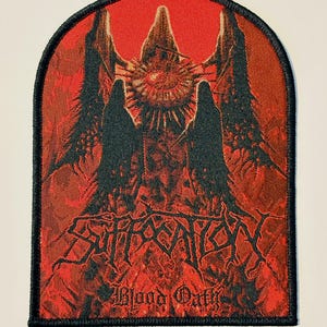 以下が含まれることがあります： ゴシックデザインの赤と黒の刺繍パッチ。「SUFFOCATION」の文字を様式化したフォントで、下に「Blood Oath」と表示。中央に詳細なイラストがあり、黒い縁取りが施されています。