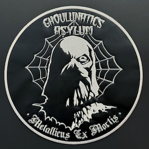 May include: A circular black and white embroidered patch featuring a ghoulish face within a spiderweb design. The text "GHOULUNATICS ASYLUM" arches across the top, with "Metallicus Ex Mortis" at the bottom. The patch has a white border.