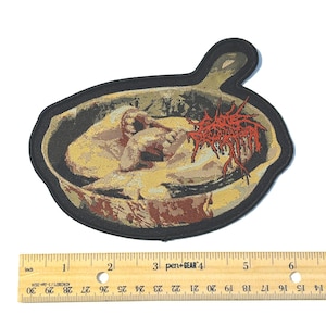 May include: Embroidered patch featuring a disturbing scene of a figure in a pan, with a red, organic-looking design. The patch has a black border and a handle shape. The image is approximately 5 inches wide.