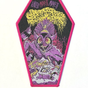 May include: A coffin-shaped embroidered patch with a bright pink border. The design features a purple creature with large red eyes, yellow textured clouds above, and the text "I LIKE TO MOVETT MOVETT" in a stylized font against a black background.