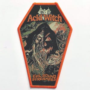 May include: An orange and black embroidered patch shaped like a coffin. The patch features a spooky illustration of a witch with a jack-o-lantern face and the text "Acid Witch Evil Sound Screamers".