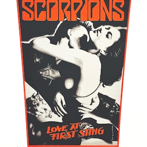 May include: A rectangular patch with a black background and a red border. The word "SCORPIONS" is in large orange letters at the top. The image depicts a couple embracing, with the text "LOVE AT FIRST STING" at the bottom.