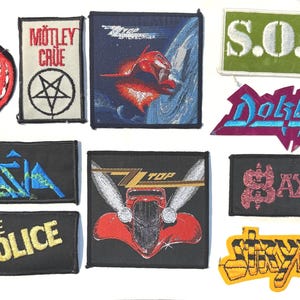 May include: A collection of embroidered patches featuring various band logos and designs. Patches include logos for Mötley Crüe, Z.Z. Top, The Police, and others. The patches are in various colors and shapes, suitable for jackets or bags.