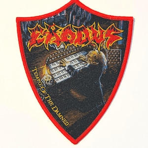 以下が含まれることがあります： 赤い縁取りのシールド型パッチ。バンド名「Exodus」が黄色と赤色の文字で表示されています。画像はオルガンを演奏する人物を描いており、「Tempo Of The Damned」というテキストが添えられています。