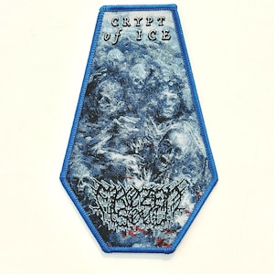 Op de afbeelding: Een blauw en wit embleem met de tekst "CRYPT of ICE" bovenaan. Het embleem toont een gedetailleerde illustratie van schedels en figuren. De onderkant van het embleem heeft meer tekst in een gotisch lettertype. Het embleem heeft een blauwe rand.