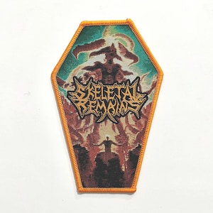 May include: A coffin-shaped embroidered patch with an orange merrowed border. The design features a dark, fiery landscape with a central figure and the text "SKELETAL REMAINS" in a stylized, jagged yellow font across the middle of the patch.