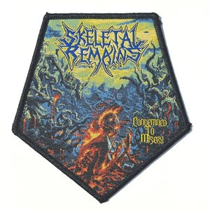 Puede incluir: Un parche bordado pentagonal con un gráfico colorido de un paisaje oscuro y ardiente en tonos azules y amarillos. El texto 'SKELETAL REMAINS' está impreso en una fuente azul dentada en la parte superior, y 'CONDEMNED TO MISERY' en amarillo a la derecha.