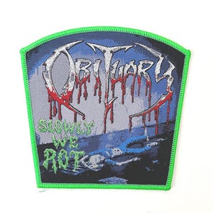 Peut inclure: Un écusson brodé trapézoïdal avec une bordure cousue vert néon vif. Le motif présente le mot OBITUARY dans une police blanche stylisée avec des gouttes rouges semblables à du sang, et le texte SLOWLY WE ROT en vert, sur une scène bleu foncé.
