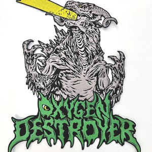May include: Green and black embroidered patch with the text "Oxygen Destroyer" and a gray monster with a yellow beam shooting from its mouth.