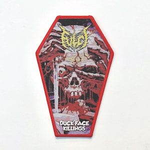 May include: A coffin-shaped embroidered patch with a red border. The design features a detailed, dark illustration of a skull with red and purple tones. At the top is a yellow stylized logo, and at the bottom, the text reads DUCK FACE KILLINGS.