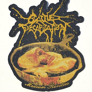 May include: A black embroidered patch featuring the yellow text Cattle Decapitation in a jagged, stylized font above an illustration of a skillet containing cooked food, with the yellow text Medium Rarities printed below the skillet.