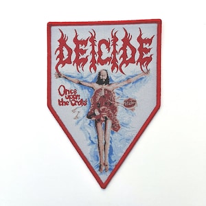 May include: A pentagonal embroidered patch featuring a red border and a light blue background. The text DEICIDE appears in red at the top, with the text Once upon the Cross in red on the left. A central figure is depicted with arms outstretched.