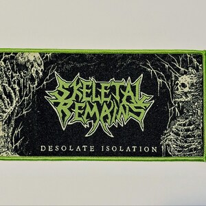 May include: A rectangular embroidered patch with a bright lime green border. The black background features a central lime green logo reading SKELETAL REMAINS, with the text DESOLATE ISOLATION below. Two skeletal figures flank the central text.