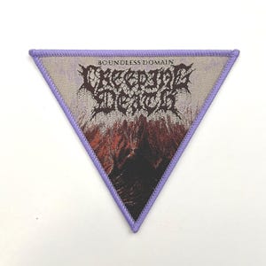 Op de afbeelding: Driehoekige patch met een paarse rand en een geweven ontwerp. De patch bevat de woorden "BOUNDLESS DOMAIN" boven de woorden "CREEPING DEATH" in een gotisch lettertype. De onderkant van de patch heeft een berglandschap in rood, zwart en grijs.