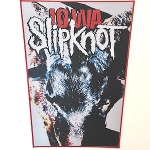 Puede incluir: Un parche rectangular con borde rojo con el nombre de la banda "Slipknot" y la palabra "Iowa" en rojo. El gráfico representa una cara de animal oscura y estilizada con tonos negros, blancos y azules.