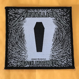 May include: Black and white woven patch with the band name "Metallica" and the album title "Death Magnetic" in a stylized font. A black coffin is in the center of the patch.