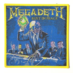 Op de afbeelding: Vierkante patch met de bandnaam "Megadeth" in geel, boven de tekst "Rust in Peace". De afbeelding toont een skeletachtige figuur in een pak die een groen object vasthoudt, met andere figuren in pakken op de achtergrond. De patch heeft een gele rand.