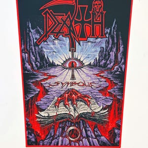 Peut inclure: Un écusson rectangulaire en tissu arborant le logo du groupe Death en rouge et noir. L'illustration représente une main griffue rouge posée sur un livre ouvert, un œil central et le mot Symbolic. Le tout sur un paysage violet.